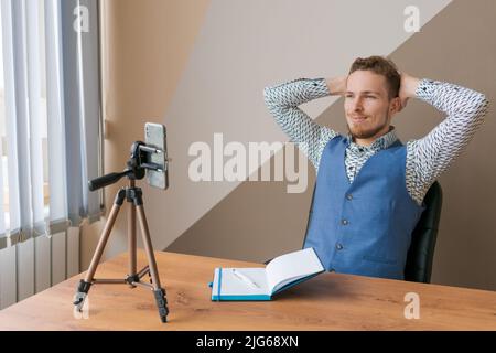 Young handsome man who is making video is making an online video call using a modern phone. Happy business people concept. Business man in the office holding a webinar Stock Photo