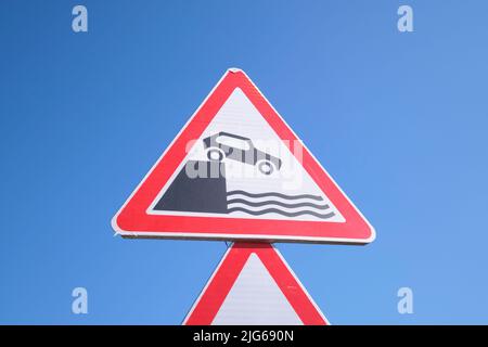 Close up, detail of the standard red and white triangle shaped metal road sign warning of driving into a canal, river, stream. Near Tashkent, Uzbekist Stock Photo