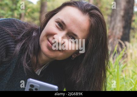 Portrait of smiling young woman in a park and looking at camera, holding smartphone Stock Photo