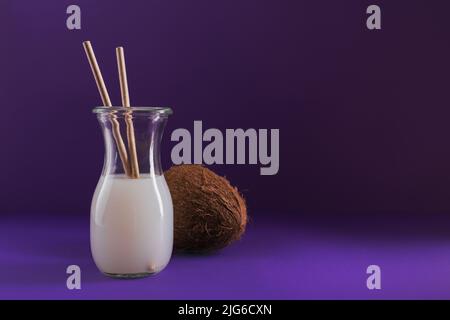 Bottle of coconut vegan milk with strews and whole coconut on purple background Stock Photo