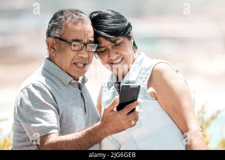 We can do so much with this. Shot of a senior couple using a phone in nature. Stock Photo