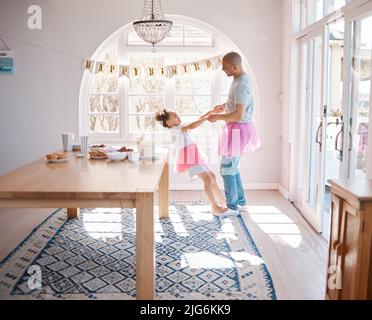 Celebrate and be your very happiest. Shot of an adorable little girl wearing a tutu and dancing with her father in the living room. Stock Photo