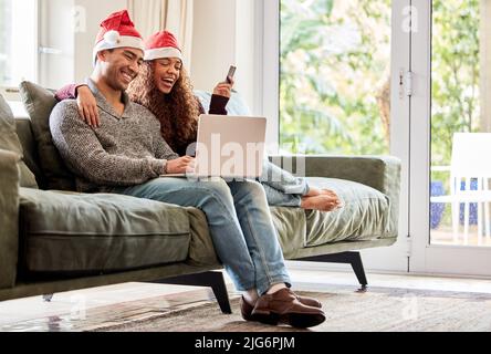 Were doing all our Christmas shopping online. Shot of a young couple doing online shopping while wearing Christmas hats at home. Stock Photo