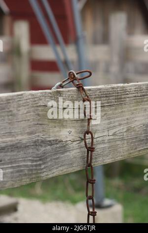 A simple rusty chain hanging on a wooden fence. Stock Photo