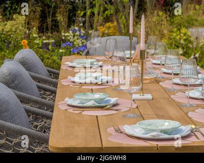 Wooden garden table set for a dinner party in a show garden at Hampton Court Palace garden Festival. London. Stock Photo