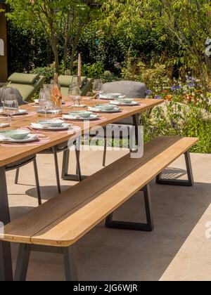 Wooden garden table set for a dinner party in a show garden at Hampton Court Palace garden Festival. London. Stock Photo