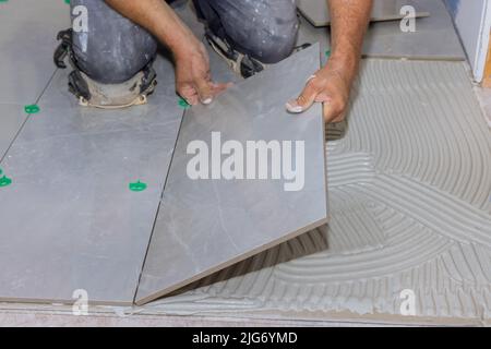 With the help of a home construction worker, placing ceramic tile on an adhesive surface Stock Photo