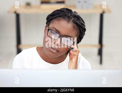 I have such a bad headache. Cropped shot of a young businesswoman using a computer while sitting at her desk. Stock Photo