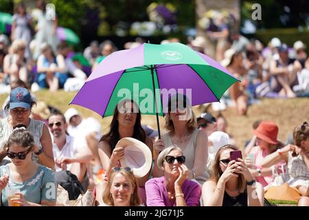 Spectators shield from the sun on day twelve of the 2022 Wimbledon Championships at the All England Lawn Tennis and Croquet Club, Wimbledon. Picture date: Friday July 8, 2022. Stock Photo