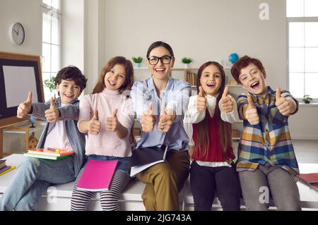 Happy smiling teacher with pupils group giving thumbs up portrait in schoolroom Stock Photo