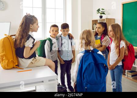Little school children have fun talking in classroom during reunion after long school vacation. Stock Photo