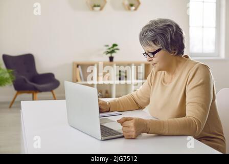 Senior woman sitting at desk and using her laptop computer for remote work or studying Stock Photo