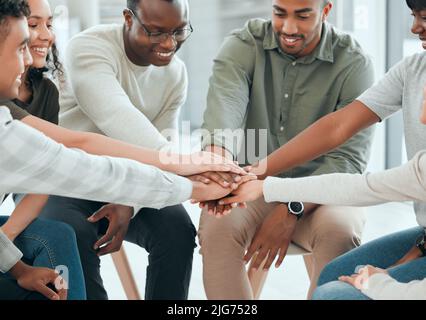 We can overcome this together. Shot of a diverse group of people sitting together and stacking their hands in the middle. Stock Photo