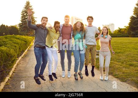 Fun group of best friends hugging and jumping up in park enjoying summer weekend. Stock Photo