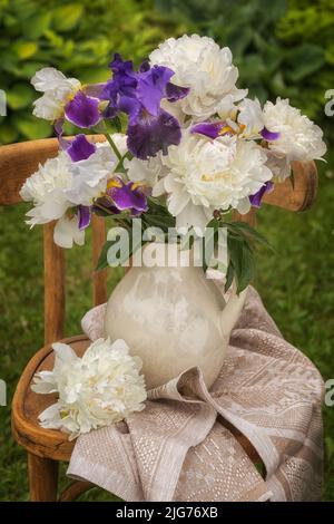 Bouquet of bearded irises and white peonies on a chair. Stock Photo