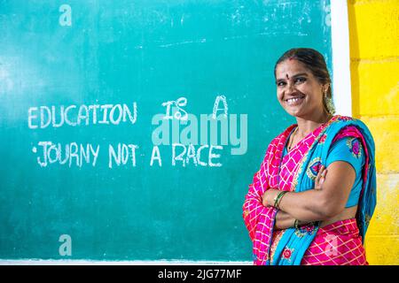 Portrait shot of happy smiling teacher with crossed arms standing in front of chalk board at classroom by looking at camera - concept of professional Stock Photo