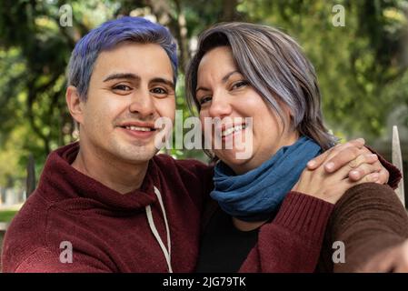 Two smiling friends are hugging and looking at camera. He has blue hair Stock Photo