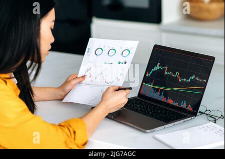 Smart successful asian female trader, stock broker, investor, analyzes growth and fall charts of cryptocurrency, online coins, predicts future performance, focused studies the market Stock Photo