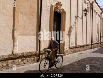 Elderly man rides his bicycle down the cobblestone streets of the Old Town of Nardo, Puglia, Italy on a hot summer day Stock Photo