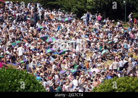 Spectators shield from the sun on day twelve of the 2022 Wimbledon Championships at the All England Lawn Tennis and Croquet Club, Wimbledon. Picture date: Friday July 8, 2022. Stock Photo