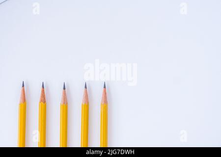 Negative space is utilized with five sharp pencils lined up on a white sheet of paper pointing upwards. Stock Photo