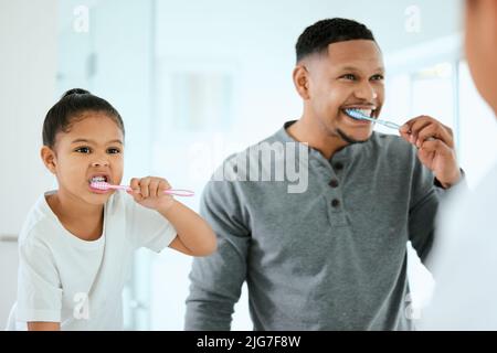Dads strict about dental. Shot of an adorable little girl and her father brushing their teeth together at home. Stock Photo