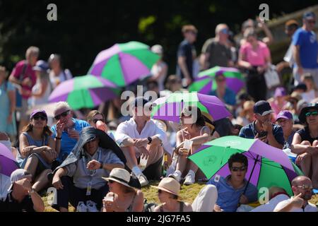 Spectators shield from the sun on day twelve of the 2022 Wimbledon Championships at the All England Lawn Tennis and Croquet Club, Wimbledon. Picture date: Friday July 8, 2022. Stock Photo