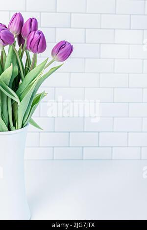 Fresh picked purple tulips in a white vase against a white subway tile kitchen background with copy space for spring background. Stock Photo