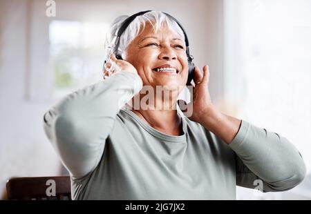 There are ways of hanging on to youth. Shot of a beautiful senior woman listening to music while sitting on the sofa at home. Stock Photo