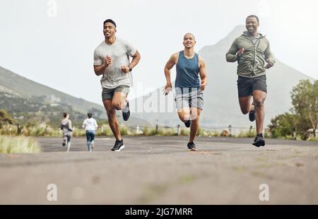 No racing, just friends motivating each other. Shot of three men out for a run on a mountain road. Stock Photo