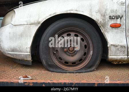 Dirty old car with a flat tyre loaded on to a truck heading for the scrap yard. Stock Photo