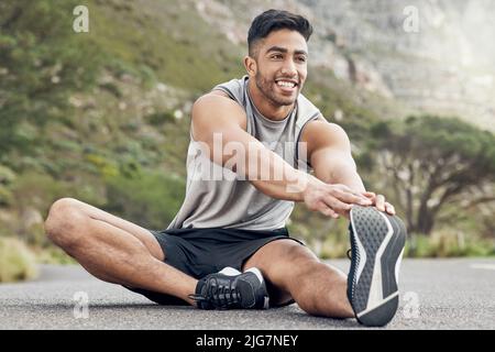Stretching is a walk in the park. Shot of an athletic young man stretching on a mountain road. Stock Photo