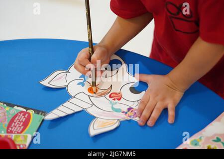 A little child coloring an animal paper mask in the classroom. Unicorn paper mask arts and crafts. Khobar, Saudi Arabia. Stock Photo