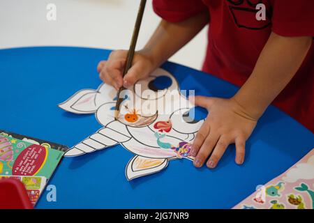 A little child coloring an animal paper mask in the classroom. Unicorn paper mask arts and crafts. Khobar, Saudi Arabia. Stock Photo