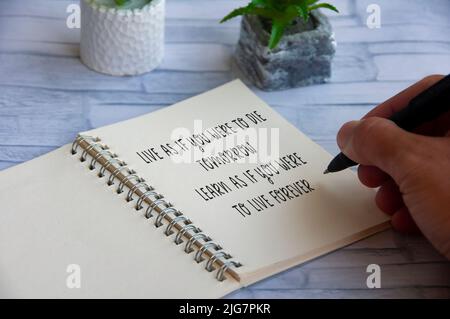 Motivational and inspirational quote- Live as if you were to die tomorrow. Learn as if you were to live forever. With hand and plant background Stock Photo