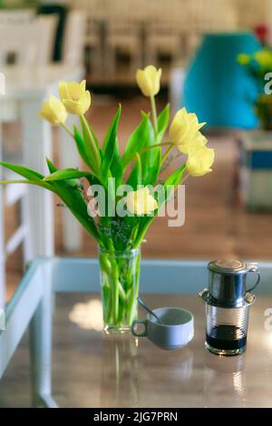 Beautiful bouquet of yellow tulips in vase on dinner table in white kitchen light interior at the home Stock Photo