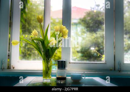 Beautiful bouquet of yellow tulips in vase on dinner table in white kitchen light interior at the home Stock Photo