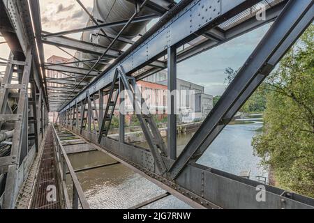 View of an abandoned power plant from a bridge with gas pipes over a river. dramatic sky Stock Photo