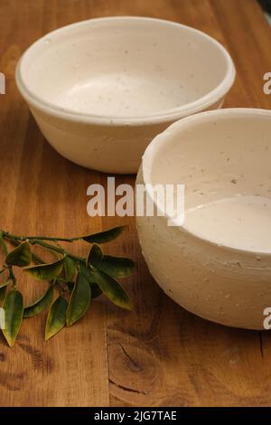 Two white empty ceramic bowls and green leaves on a wooden table Stock Photo