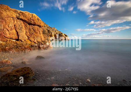 Scenic landscape of a small beach on the coast of Cartagena, Spain, taken with long exposure in which the colors of the rocks, the sea and the sky sta Stock Photo