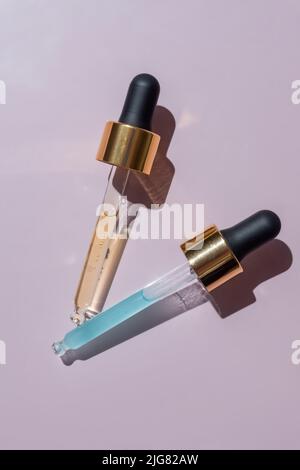 Transparent pipettes with blue and yellow cosmetics serum on a light pink background. Product texture. Dropper glass bottle branding mockup. Cosmetic Stock Photo