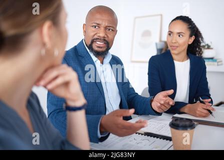 Diverse group of business people talking in a meeting and using technology and paperwork in a boardroom. Team of professionals sitting together Stock Photo