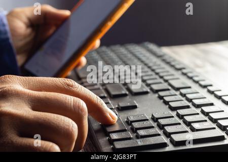 Selective focus on an Indian male hand using mobile phone to enter one time password in front of computer Stock Photo