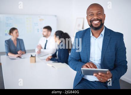 Portrait of smiling confident african american businessman in boardroom using digital tablet. Diverse group of businesspeople in meeting and working Stock Photo