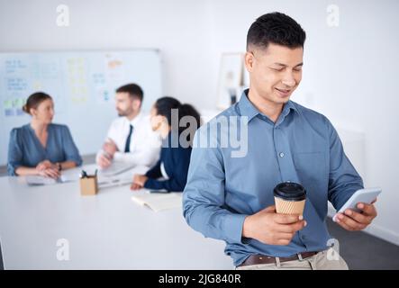Smiling confident mixed race businessman in boardroom using cellphone. Diverse group of businesspeople in meeting and working behind hispanic manager Stock Photo