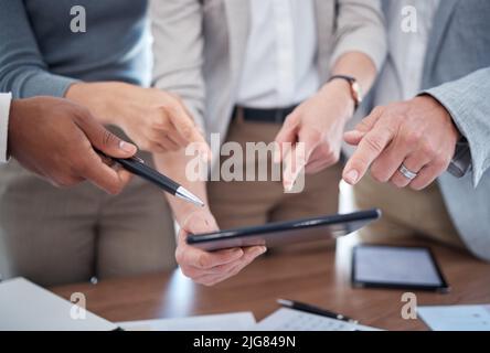 They have so many questions. Cropped shot of a group of unrecognizable businesspeople looking over a tablet in the boardroom. Stock Photo