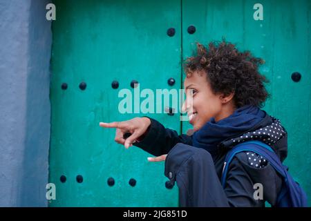 An African-American woman pointing with fingers with surprised look near the green door Stock Photo