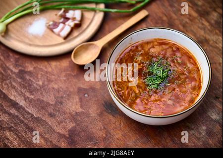 Ukrainian national dish: red beetroot soup - traditional tasty Borscht with parsley and dill, chopped bacon, salt and green onions nearby on a wooden Stock Photo