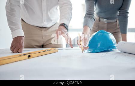 Making sure the plans are up to code. Cropped shot of two unrecognizable architects looking over blueprints in the office. Stock Photo