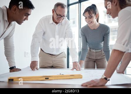Going over the blueprints. Cropped shot of four architects looking over blueprints in the office. Stock Photo